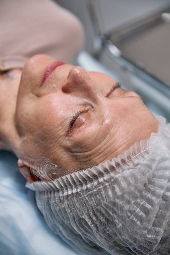 Elderly woman with eyes closed in hospital setting, wearing hairnet.